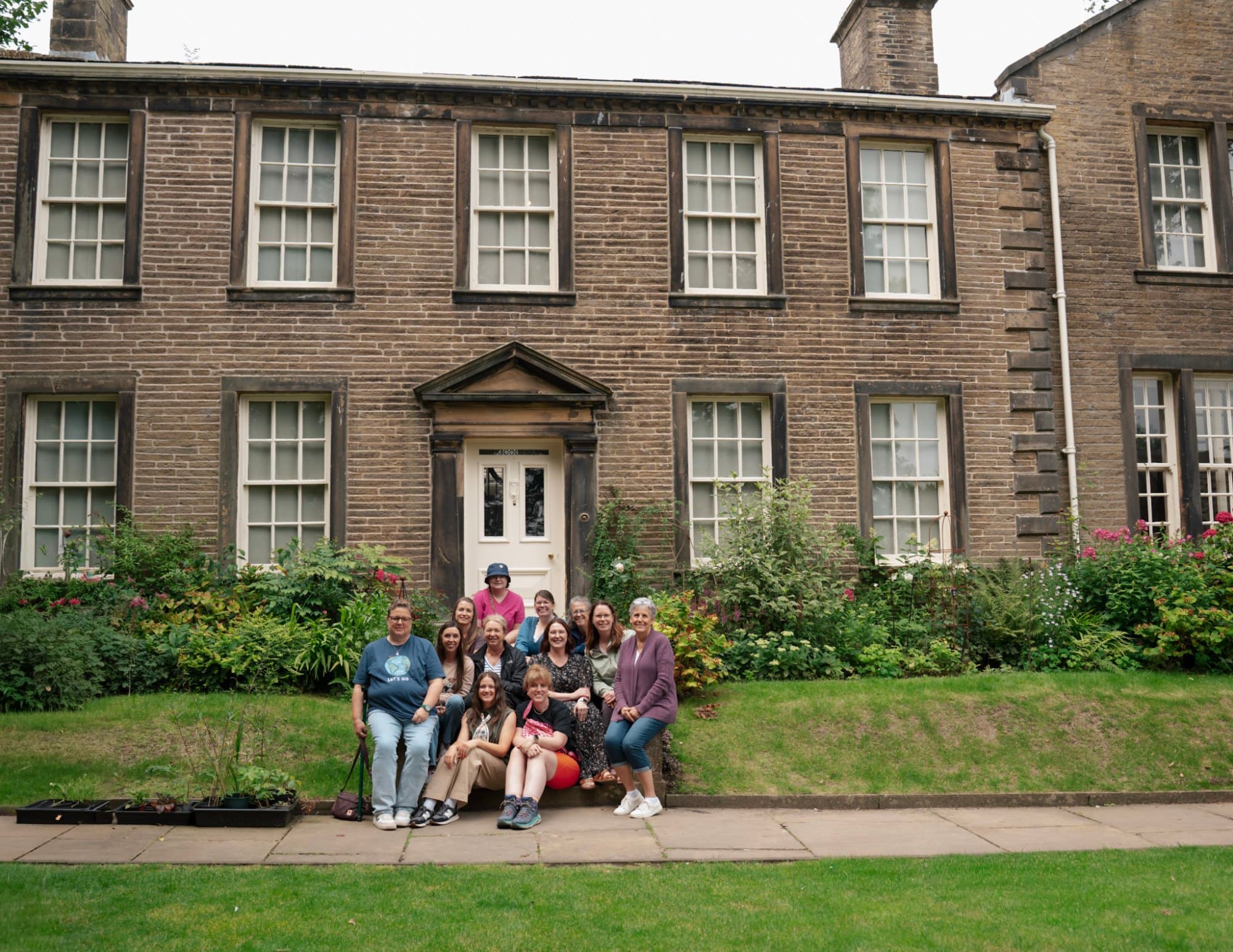 a group of women sitting in front of the bronte parsonage museum in haworth england on the book club tour