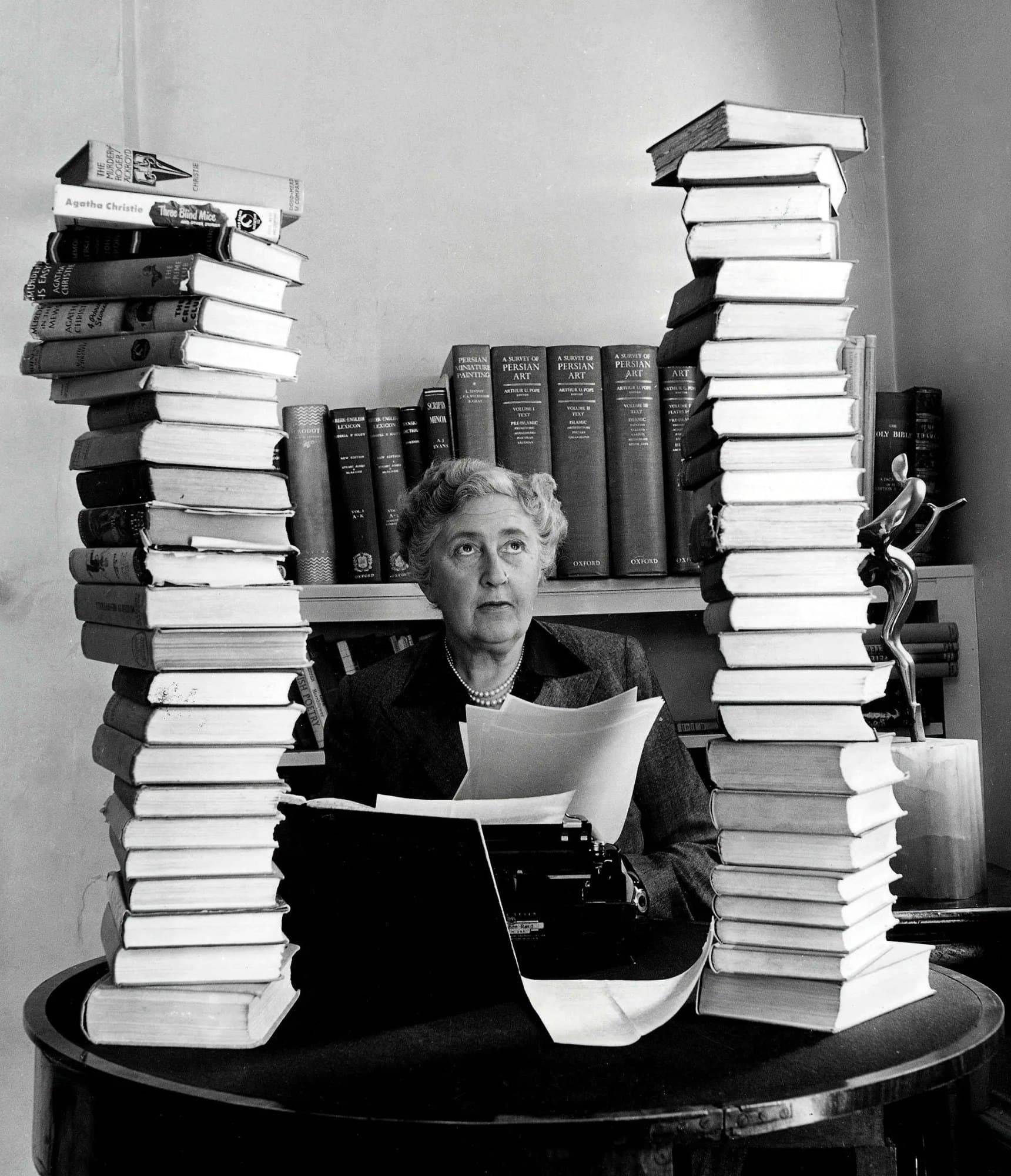 Black and white photo of Agatha Christie later in life surrounded by stacks of books