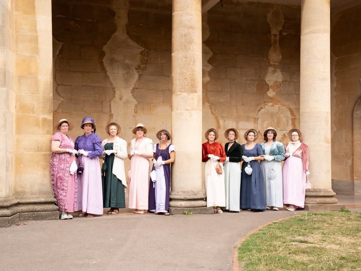 a group of women dressed in regency period attire posing by columns in Bath